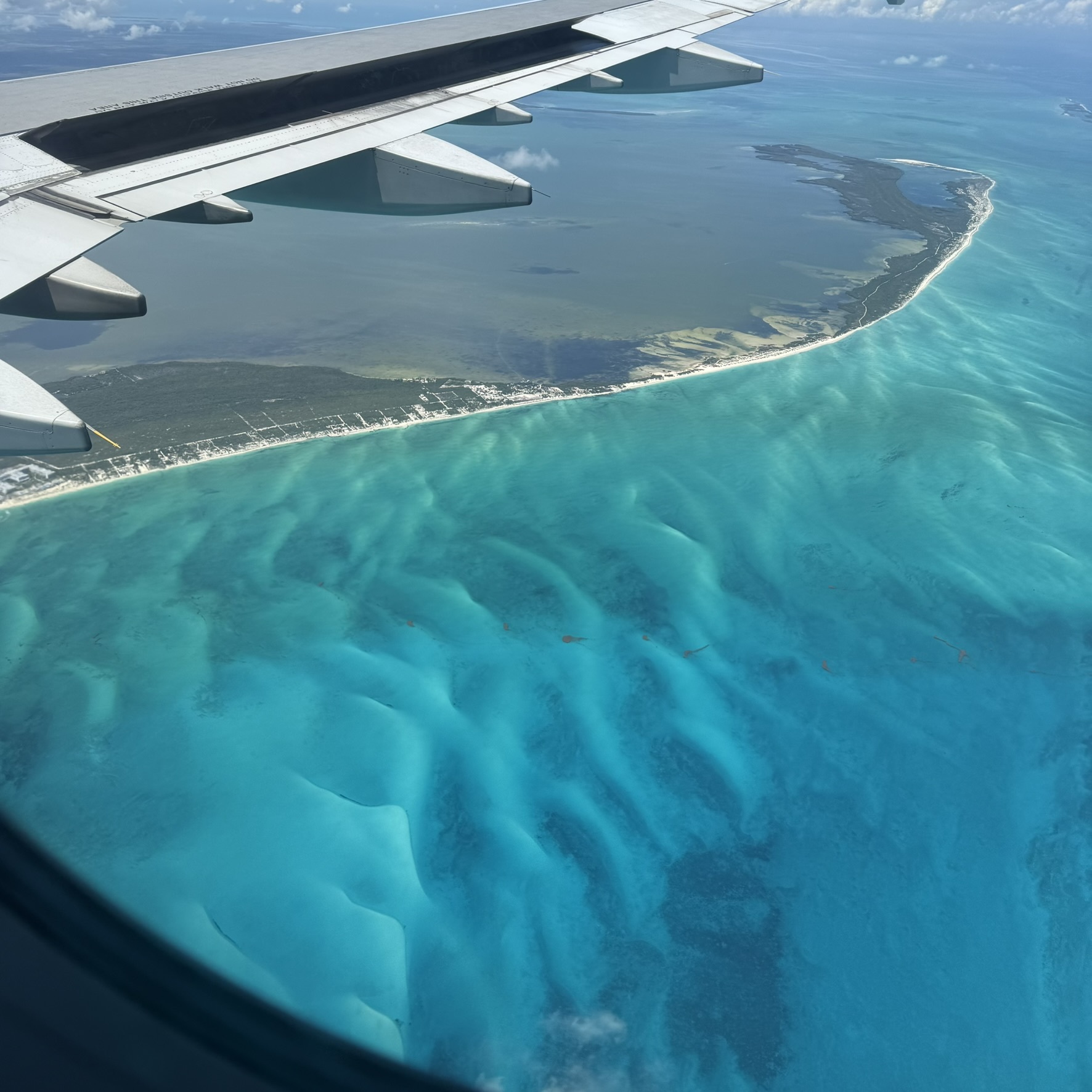View from an airplane window of the wing over turquoise Caribbean water while flying into Cancún, Mexico.