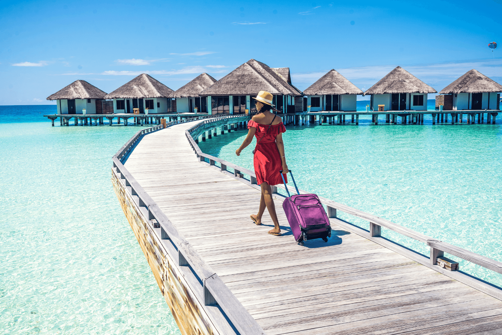Woman walking with a suitcase to a resort with houses on the water
